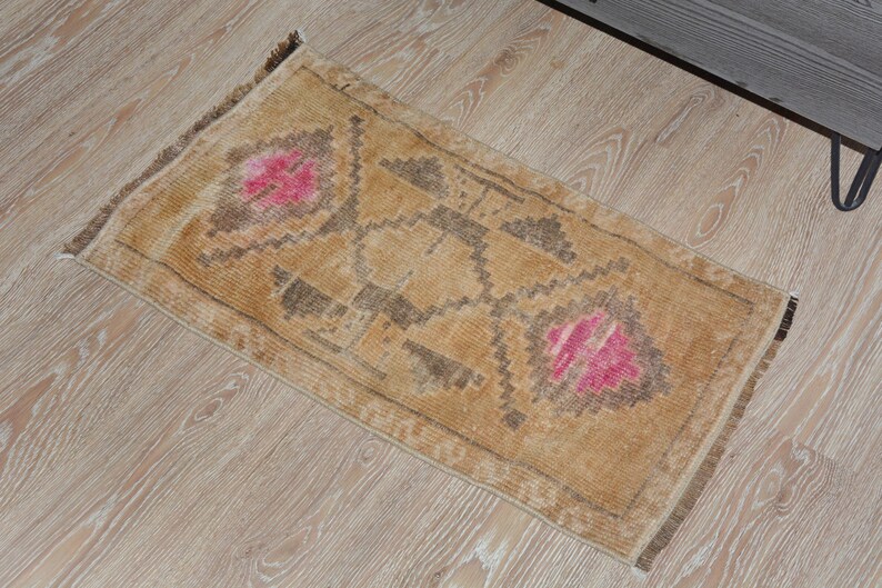 Puede incluir: Una alfombra rectangular de estilo vintage, en tonos beige y marr&oacute;n. La alfombra presenta un dise&ntilde;o central con elementos florales rosas y patrones geom&eacute;tricos. Est&aacute; colocada sobre un suelo de madera clara.