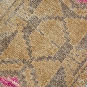 Puede incluir: Primer plano de una peque&ntilde;a alfombra rectangular con un patr&oacute;n geom&eacute;trico. La alfombra presenta un dise&ntilde;o repetitivo en tonos beige, marr&oacute;n y rosa. La textura parece suave y tejida, lo que sugiere un estilo hecho a mano o tradicional.