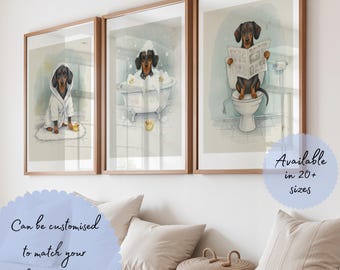 May include: Three framed wall art prints featuring a dachshund in a bathroom setting. The first shows the dog in a white bathrobe, the second in a bubble bath, and the third sitting on a toilet reading a newspaper. Each print has a light background.
