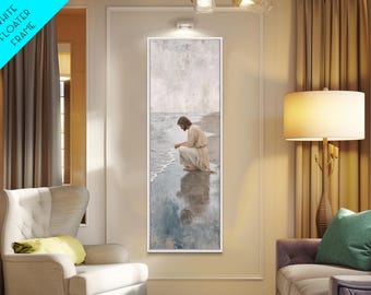 May include: A framed vertical art print depicts a person in light-colored robes kneeling at the water's edge. The artwork features a muted color palette of grays, blues, and beige, with a white floater frame. The image evokes a sense of serenity.