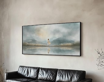 May include: A framed landscape art print depicts a figure in a white robe walking on water, with a mountain range in the background. The artwork has a muted color palette of blues, greens, and beige, and is displayed above a black leather sofa.