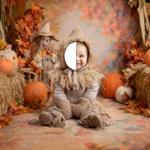 May include: A baby dressed in a scarecrow costume sits in a fall-themed setting. The scene includes pumpkins, hay bales, and a scarecrow figure. The background features autumn foliage and a warm color palette.