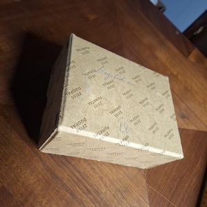 May include: A folded cardboard box with the text "ZEISS PUNKTAL DUOPAL UMBRAL" printed repeatedly in a pattern. The box is brown and sits on a wooden surface.