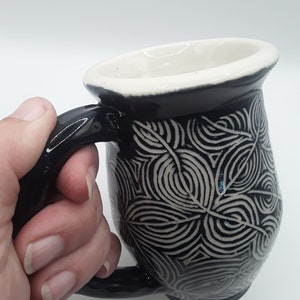 May include: Black ceramic mug with a white geometric pattern. The mug has a rounded body and a black handle.