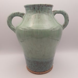 May include: A light green ceramic vase with two handles. The vase has a speckled glaze and a brown base.