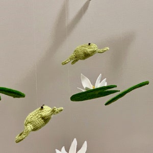 May include: A green felt frog mobile with white felt lily pads and flowers hanging from a branch.