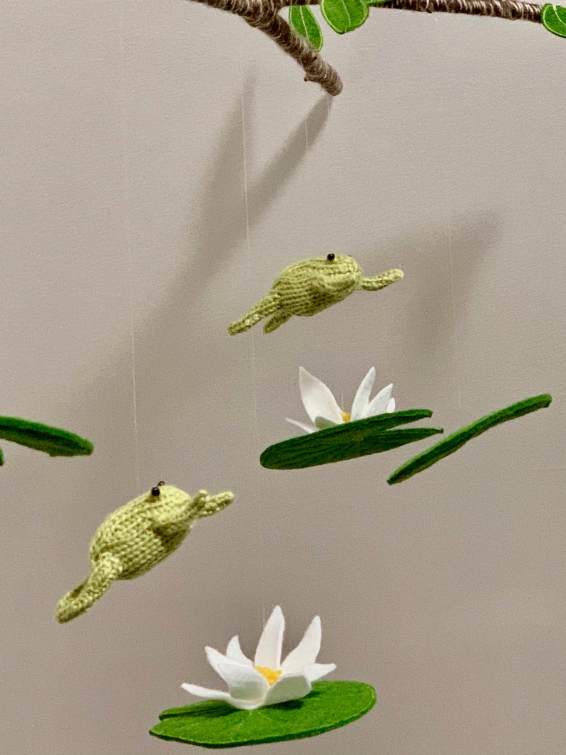 May include: A green felt frog mobile with white felt lily pads and flowers hanging from a branch.