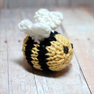 Könnte beinhalten: Ein gestricktes Bienens Spielzeug mit gelben und schwarzen Streifen und weißen Flügeln. Die Biene hat ein braunes Gesicht mit zwei schwarzen Augen.