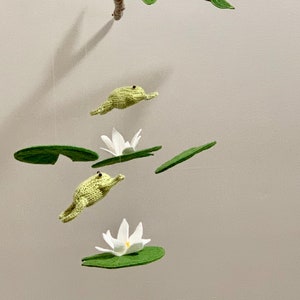 May include: A green felt mobile with three frogs and three lily pads. The frogs are jumping and the lily pads have white flowers.