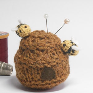 May include: A brown crocheted beehive pincushion with two yellow and black crocheted bees and two pearl-headed pins.