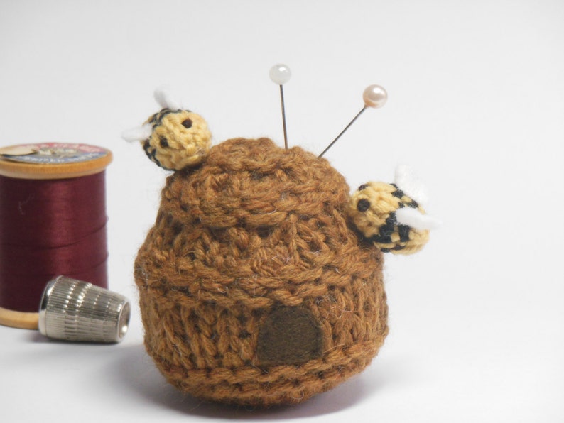 May include: A brown crocheted beehive pincushion with two yellow and black crocheted bees and two pearl-headed pins.