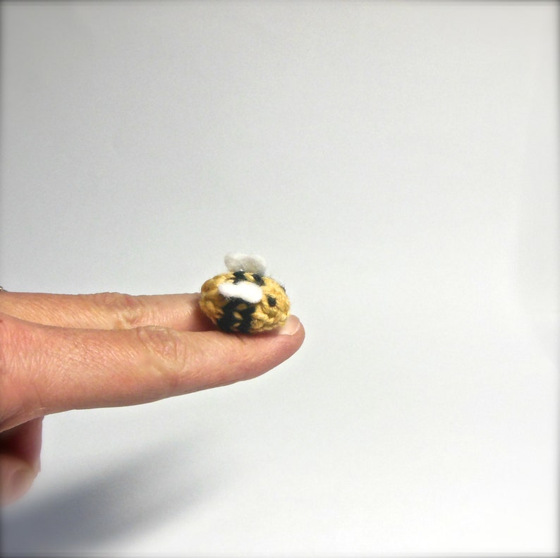 May include: A small crocheted bee with yellow and black stripes and white wings. The bee is about the size of a fingertip.