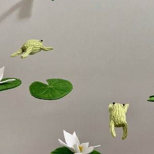 May include: A mobile with green felt lily pads and white felt lily flowers, and green knitted frogs hanging from the ceiling.