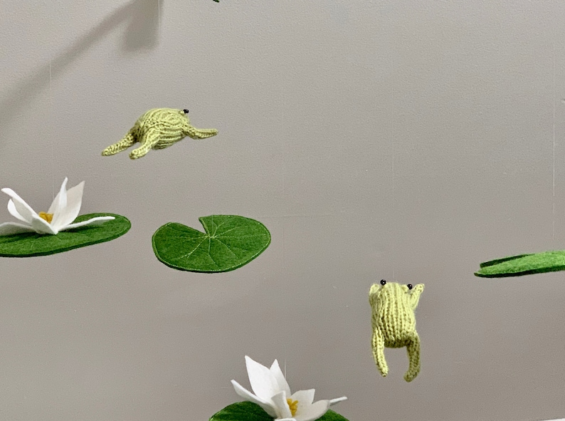 May include: A mobile with green felt lily pads and white felt lily flowers, and green knitted frogs hanging from the ceiling.