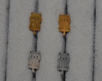 Puede incluir: Dos pares de pendientes con forma de gato. El par superior es de tono dorado y el par inferior es de tono plateado. Cada pendiente presenta una cara grabada sencilla con bigotes, orejas pequeñas y una cola en metal liso.