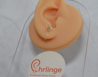 Op de afbeelding: Een goudkleurige stervormige oorbel met een centrale heldere steen, bevestigd aan een doorzichtige plastic clip-on achterkant. De oorbel wordt getoond op een beige oormodel met een rond wit label met de tekst Chrlinge Schmuck ohne Stich.