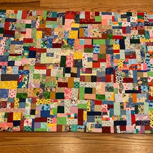 May include: A handmade patchwork quilt with a vibrant array of fabric squares in various colors and patterns. The quilt features a mix of floral, geometric, and abstract designs, creating a visually rich and textured piece.