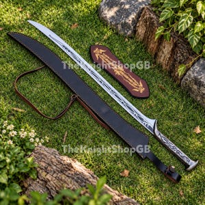 May include: A long, curved silver sword with intricate black engravings along the blade and handle. It is accompanied by a black leather scabbard featuring a brown leather strap and a separate, smaller brown leather sheath with gold-coloured detailing.