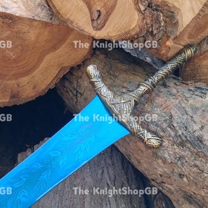 May include: A sword with a bright blue blade featuring an etched leaf pattern and a textured, antique brass-coloured metal hilt. The hilt has a crossguard and a twisted grip design. The text The KnightShopGB is visible across the image.