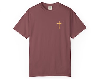 May include: A maroon t-shirt featuring a small, yellow cross emblem on the left chest. The short-sleeved top has a crew neck and a tag at the back of the neck. The shirt is made of a soft material.
