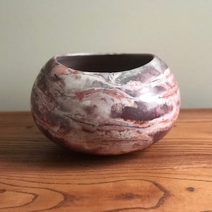 Pode incluir: Uma tigela redonda de cerâmica com um design marmorizado em tons de marrom, rosa e branco.