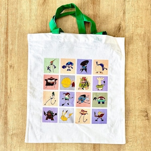 May include: White tote bag with green handles featuring a grid of colorful cartoon characters. Each character is set against a different pastel-colored square. The bag is made of a sturdy fabric.
