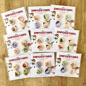Puede incluir: Múltiples paquetes de insignias "IMPOSSTARS". Cada paquete contiene cuatro insignias de personajes de juegos retro únicos. Las insignias presentan ilustraciones de dibujos animados coloridos sobre un fondo crema, con una variedad de diseños y colores.