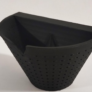 Könnte beinhalten: Ein schwarzes, kegelförmiges Objekt mit flacher Oberseite und perforiertem Unterteil. Das Objekt hat ein einzigartiges, eckiges Design und scheint aus einem matten Material zu bestehen. Der Innenraum ist sichtbar und zeigt eine dreieckige Form.