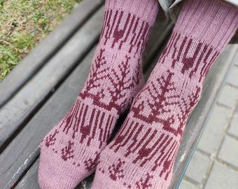 May include: A pair of mid-calf knit socks in a soft dusty pink color featuring a dark maroon geometric pattern that resembles stylized evergreen trees. The socks have a ribbed cuff at the top and a smooth knit texture throughout the foot and ankle.