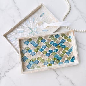 May include: Two rectangular trays with mother-of-pearl inlay. The top tray features a white floral petal pattern and a matching spoon. The bottom tray displays a multi-colored scalloped pattern in shades of blue, green, and beige.