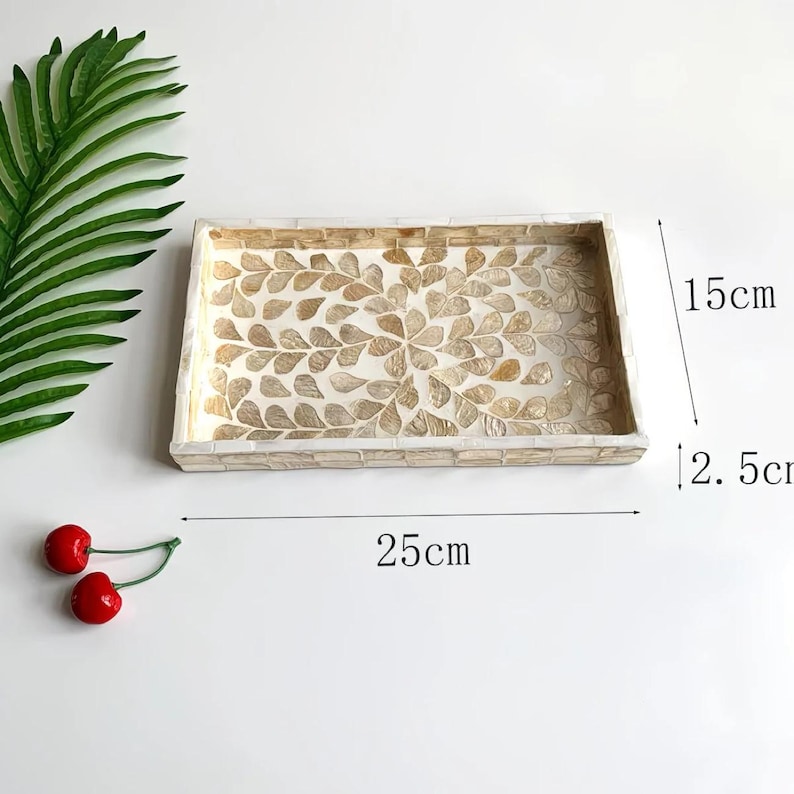 Pode incluir: Bandeja decorativa retangular, com 25 cm de comprimento, 15 cm de largura e 2,5 cm de profundidade. A bandeja apresenta um design de mosaico com um padr&atilde;o de folhas em tons de bege e creme. A borda &eacute; feita de pequenas pe&ccedil;as retangulares.