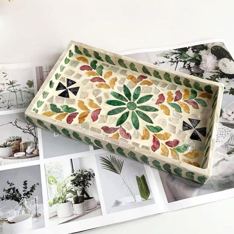 Pode incluir: Bandeja decorativa retangular com um design de mosaico. A bandeja apresenta um padr&atilde;o floral verde central rodeado por formas de folhas coloridas em vermelho, amarelo e verde. A borda &eacute; contornada com pequenas pe&ccedil;as de mosaico verdes.