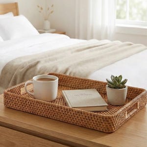 May include: A rectangular woven rattan tray with a white mug, a small book, and a potted succulent. The tray is on a wooden surface, with a bed in the background.