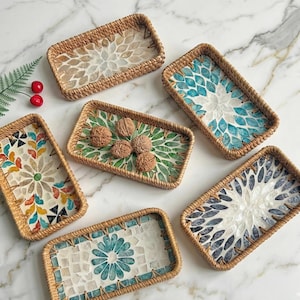 May include: A collection of rectangular woven trays with decorative mosaic tile inserts. The trays feature floral and geometric patterns in various colors, including blue, green, and beige. Some trays hold walnuts. The trays are arranged on a marble surface.