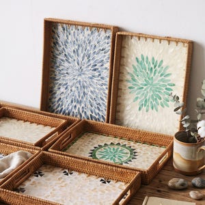 May include: A collection of rectangular woven rattan trays featuring decorative inlaid patterns. Two trays stand upright displaying blue and green petal designs, while three horizontal trays show intricate floral and geometric shell mosaics.