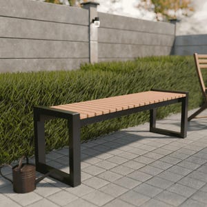 Peut inclure: Banc d'extérieur moderne avec une assise à lattes marron clair et un cadre en métal noir. Le banc est posé sur un patio carrelé gris, avec une haie verte et un mur en béton en arrière-plan. Un petit arrosoir marron est au sol.