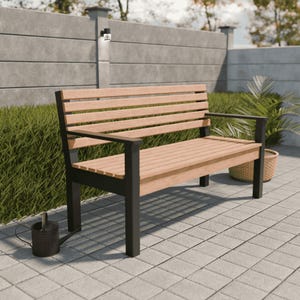 Op de afbeelding: Een houten tuinbank met een lattenrug en zitting, ondersteund door zwarte metalen poten en armleuningen. De bank is lichtbruin en staat op een grijze betegelde patio. Een kleine gieter staat op de grond bij de bank.