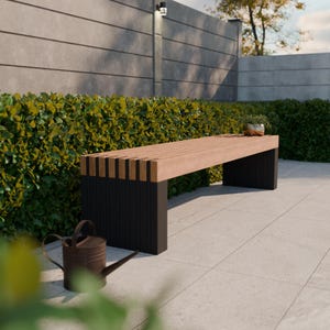 Pode incluir: Um banco moderno para exteriores com assento de ripas castanho claro e pernas pretas. O banco está colocado em frente a uma sebe verde e a uma parede de betão cinzento. Um pequeno regador está em primeiro plano.