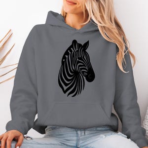 May include: A gray hooded sweatshirt featuring a black zebra head design. The zebra graphic is centered on the front of the sweatshirt. The sweatshirt has a kangaroo pocket and a drawstring hood. The design is a simple, yet striking, graphic.
