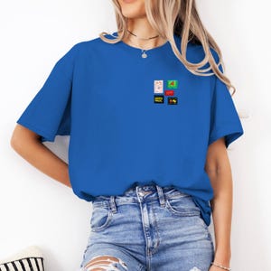 May include: A royal blue t-shirt with a small, colorful graphic design on the chest. The design includes several small images with text, including "Pasta Dept.". The shirt is made of a soft material and has short sleeves.