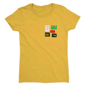May include: Mustard yellow t-shirt with a crew neck. The shirt features several small, colorful graphic designs, including text that reads "pasta dept.". The designs are in various shapes and colors, adding visual interest to the shirt.