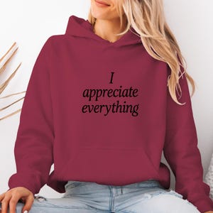 Może przedstawiać: Bordowa bluza z kapturem z czarnym napisem "I appreciate everything". Bluza z kapturem ma kaptur ze sznurkiem i przednią kieszeń. Tekst jest prostą, elegancką czcionką.