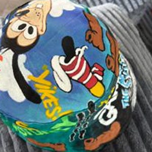 Può includere: Un cappello a secchiello multicolore con un disegno dipinto a mano del personaggio dei cartoni animati Pippo su sfondo blu. Il cappello include il testo giallo YIKES e altri elementi grafici come un calzino a righe rosse e bianche.