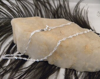 May include: A silver chain necklace with a twisted design. The chain is lying on a light grey rock.