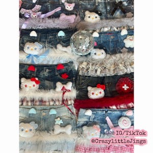 May include: A collage of denim skirts and shorts adorned with plush Hello Kitty faces, bows, and decorative trim. A disco ball and various embellishments are interspersed throughout the display. The image includes the Instagram and TikTok handle @CrazyLittleJings.