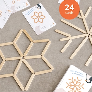 May include: A set of 24 cards with snowflake designs and wooden craft sticks. The cards feature illustrations of snowflakes and instructions. The image includes a completed snowflake made from craft sticks.