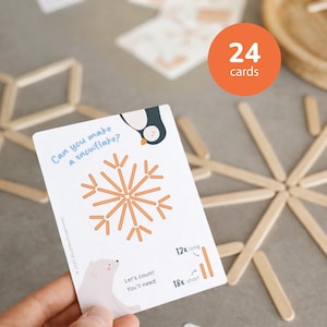 May include: A white card with the text "Can you make a snowflake?" features a snowflake diagram made of wooden sticks. The card also includes a penguin and polar bear illustration, and the text "24 cards".