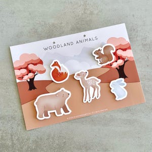 May include: A set of woodland animal stickers on a card. The stickers include a fox, bear, deer, squirrel, and rabbit. The card has a brown and white background with trees and the words "Woodland Animals".