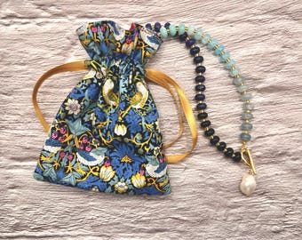 May include: A blue drawstring bag with a floral and bird pattern, and a gold cord. A beaded necklace with dark blue, light blue, and clear beads, and a pearl pendant.