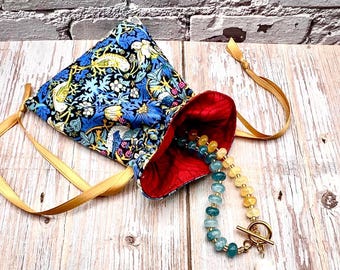 May include: A blue floral drawstring pouch with a red interior, gold ribbon ties, and a beaded necklace with a gold clasp. The pouch features a pattern of birds, flowers, and leaves.